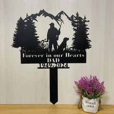 a metal memorial sign with a silhouette of a man and his dog on it, next to a potted plant