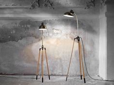 two floor lamps sitting next to each other on top of a wooden tripod stand