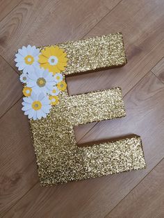 the letter e is decorated with daisies and daisies in gold glitter, on a wood floor