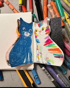 an open book with colored crayons next to it and a drawing of a cat