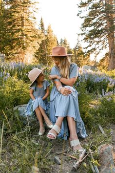 mother and daughter sitting on the ground in front of trees with bluebells behind them