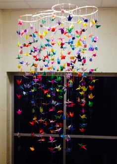 a wind chime with colorful paper cranes hanging from it's sides in front of a window