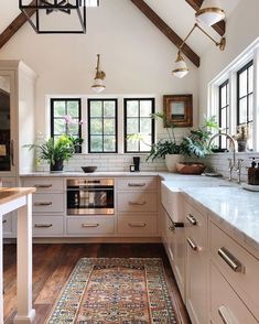 a kitchen with lots of white cabinets and wooden floors, along with a rug on the floor