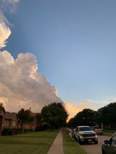 cars parked on the side of a road in front of some houses with clouds above them