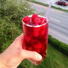 a person holding up a glass filled with raspberries on the side of a road