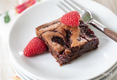 two pieces of brownie with raspberries are on a plate next to a fork