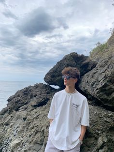 a young man standing on top of a rocky beach next to the ocean wearing sunglasses