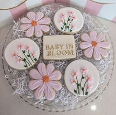 baby in bloom decorated cookies on top of a glass platter with pink daisies