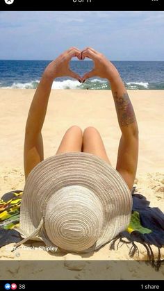 a woman laying on top of a sandy beach holding a heart shaped object in her hands