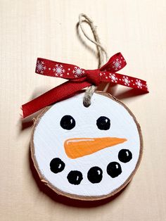 a wooden ornament with a snowman face on it's side hanging from a red ribbon