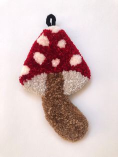 a red and white knitted mushroom ornament hanging from a black hook on a white background