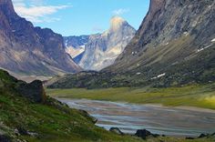 the mountains are covered in snow and green grass, with a river running between them