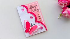 a pink and white birthday card with a butterfly on it, next to some flowers