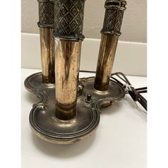 three brass candlesticks are on a stand with wires plugged into the wall