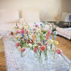 flowers are arranged in vases on a glass coffee table with white furnishing