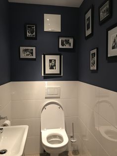 a white toilet sitting in a bathroom next to a sink and framed pictures on the wall