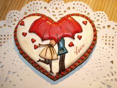 a heart shaped cookie with an image of a man and woman under an umbrella on it