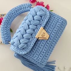 a crocheted blue purse sitting on top of a white table next to pink flowers