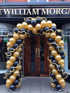 an arch made out of black and gold balloons in front of a store with the name william morgan on it