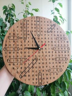 a wooden clock with words and numbers on the face, in front of some leaves