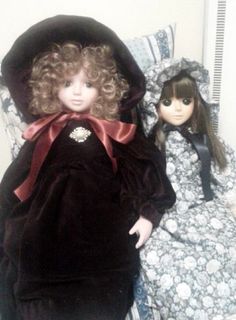 two dolls sitting next to each other on a bed