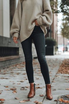 A chunky sweater paired with dark skinny jeans creates the perfect fall look.  The neutral-toned sweater balances the darker tones of the outfit, while the sleek brown ankle boots add a modern touch.  This combination works for casual outings or city strolls, giving you both comfort and style in the changing weather. Fall Jeans Outfit Casual Ankle Boots, Brown Ankle Boots Outfit Fall, Dark Jeans Outfit Fall, Brown High-top Booties For Fall, Trendy Brown Ankle-high Martin Boots, Trendy Brown High-ankle Mid-calf Boots, Chic Brown Ankle-high Martin Boots, Black Jeans Brown Boots, Dark Brown Boots Outfit