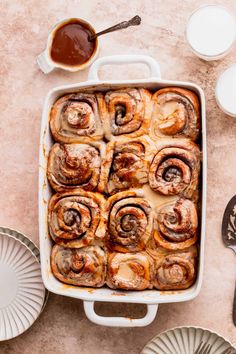 a baking dish filled with cinnamon rolls on top of a table next to plates and utensils