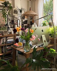 a desk with a laptop and flowers in a vase