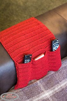 two remote controls in a red knitted case on a leather couch with a black armrest