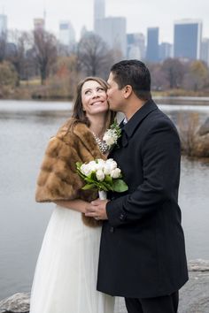 a bride and groom standing next to each other in front of a body of water