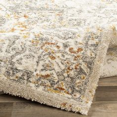 a white rug with yellow and gray flowers on the bottom is laying on top of a wooden floor