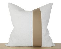 a white pillow with a brown stripe on the front and back side, sitting on a wooden table