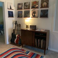 a room with guitars on the wall and various pictures hanging above it, along with a striped rug