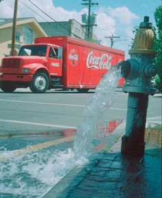 a fire hydrant spewing water out of it's side in front of a coca - cola truck