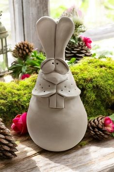 a white vase sitting on top of a wooden table next to pine cones and flowers