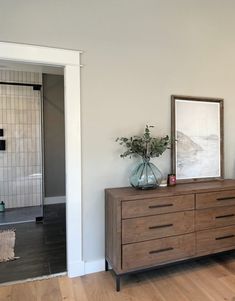 a room with a dresser, mirror and vase on the table in front of it