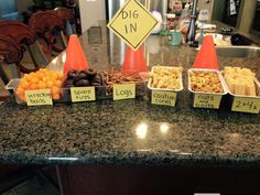 a counter topped with lots of different types of food next to orange cones and signs