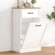 a white cabinet with an open door next to a potted plant on the floor