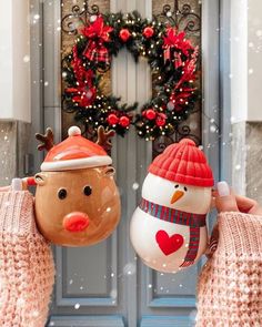 two snowmen with hats and scarves holding up mugs in front of a door