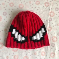 a red knitted beanie with white and black letters on it sitting on top of a bed