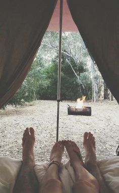 two people are laying in bed under an umbrella with the view of a campfire