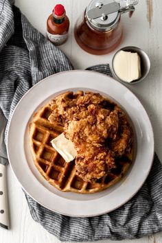 fried chicken and waffles on a white plate next to butter, syrup and sauce