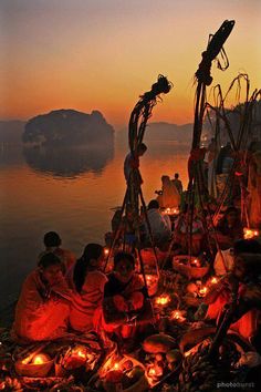 people sitting on the ground with candles in front of them and water behind them at sunset