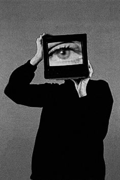 a man holding up a television with an eye on it's screen in front of his head