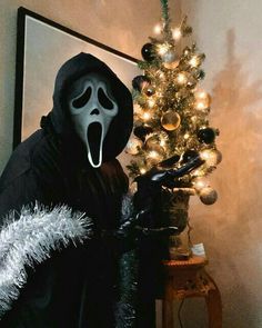 a person wearing a ghost mask next to a christmas tree