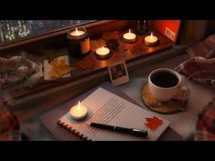 a cup of coffee and some candles on a table next to a book with writing paper