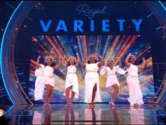 four women in white dresses on stage with their arms up and hands raised to the side