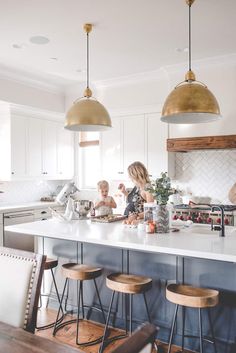 a woman standing in a kitchen next to two stools and a counter with food on it