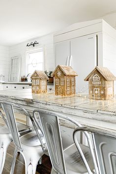 the kitchen counter has three little houses on it and four chairs are in front of them