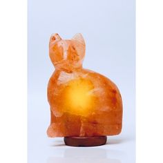 an orange glass cat sitting on top of a wooden stand next to a white background